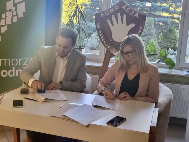 podpisanie umowy, dwie osoby, w tle roll-up z zielonym tłem, napis Pomorze Zachodnie