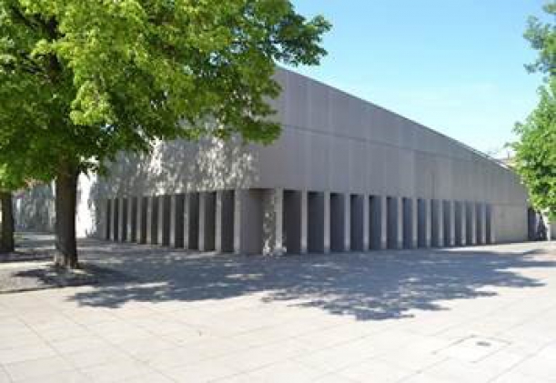 betonowa bryła prostokątnego budynku muzeum w cieniu drzew.