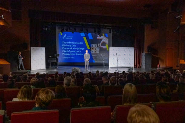 marszałek województwa Olgierd Geblewicz, przed marszałkiem siedzi publiczność, goście uroczystości, w tle niebieski napis z nazwą uroczystości