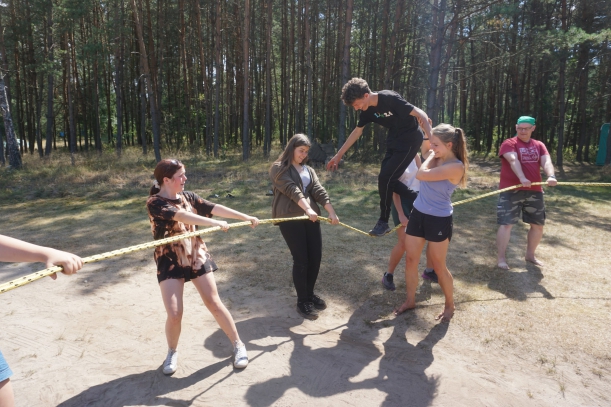 uczestnicy trzymają napięty w kręgu pas po którym idzie kolega asekurowany przez trenera