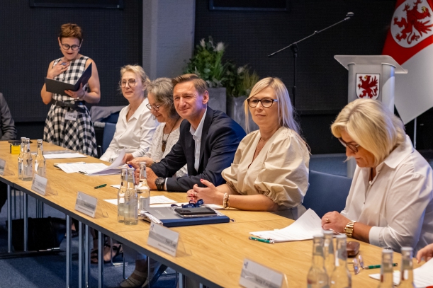 za stołem w sali kina Delfin siedza goście sptkania, na pierwszym planie wicemarszałkini Anna Bańkowska i marszałek Olgierd Geblewicz