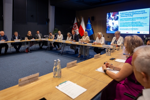 za stołem ustawionym w kształcie litery C siedza goście spotkania  w sali kina delfin