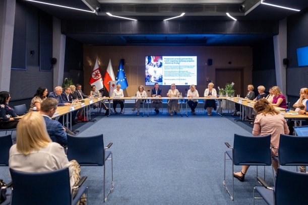 za stołem ustawionym w kształcie litery C siedza goście spotkania  w sali kina delfin