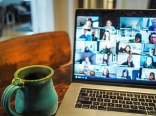 otwarty laptop na stoliku, obok kubek z napojem. Na ekranie twarze osób podłączonych do spotkania on-line